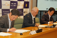 〈写真：協定書に署名する、（左から）小村社長、山下学長、飯塚市長＝１日、出雲市西林木町の県立大学出雲キャンパス〉  　