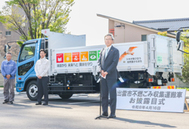 〈写真：トキのラッピングが施されたトラックの前であいさつする足立佐年社長（右）＝16日、出雲市役所〉