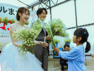 〈写真：地元保育園児からカモミールの花束を受け取る新郎新婦＝１日、大田市波根町の旭養鶏舎〉
