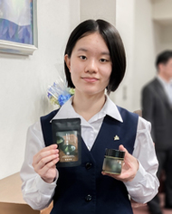 〈写真：自ら開発した「まるで抹茶」を手にする岩本さん＝15日、松江市殿町の県庁〉