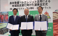 〈写真：協定書を手に、左からプロテリアル安来工場の渡辺工場長、糸原町長、バイウィルの下村社長＝15日、奥出雲町役場仁多庁舎〉