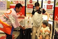 〈写真：隠岐世界ジオパーク空港からの乗客に就航60周年の記念品を手渡す飯塚俊之市長（左）＝５日、出雲市斐川町沖州の出雲縁結び空港〉