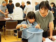 〈写真：神西湖の水質調査を行う参加者＝22日、出雲市古志町の古志コミュニティセンター〉