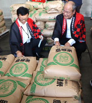 〈写真：「たたら焔米・雲南市認証」シールを貼る石飛市長（右）と源本部長＝16日、雲南市大東町飯田のＪＡしまね雲南地区本部大東農業倉庫〉